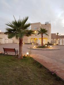 un banco de parque y palmeras frente a un edificio en منتجع القصر الأبيض, en Unaizah