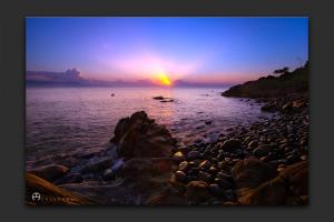 a sunset over a rocky beach with the ocean at Quy Nhon Homestay BnB in Quy Nhon