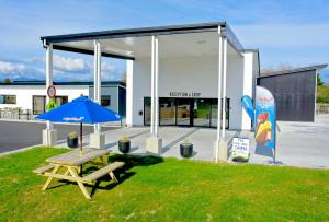 a picnic table with a blue umbrella in front of a building at Hokitika's Kiwi Holiday Park and Motels in Hokitika