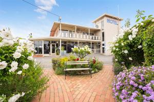 um banco sentado em frente a um edifício com flores em Best Westlander Motor Inn em Horsham