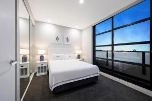 a bedroom with a white bed and a large window at The Hamptons Apartments - St Kilda in Melbourne