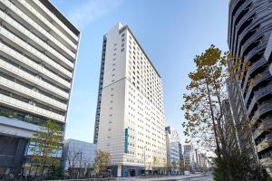 a tall white building in the middle of a city at Sotetsu Fresa Inn Higashi Shinjuku in Tokyo