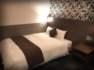 a hotel room with a bed with white sheets and pillows at Sejour Inn Nagarekawa in Hiroshima