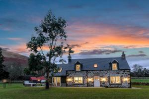 una casa de piedra con una puesta de sol en el fondo en Dalveich Cottage, hot tub, 2 bedroom, Lochearnhead en Lochearnhead