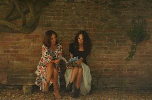 Duas mulheres sentadas numa parede a ler um livro. em Relais Alcova del Doge em Mira