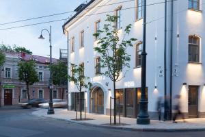 a street with a white building and trees on the sidewalk at Somnia Apartments in Vilnius