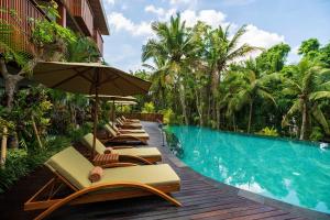 a row of lounge chairs and an umbrella next to a swimming pool at Adiwana Unagi Suites in Ubud