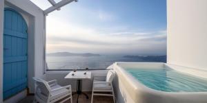 a balcony with a bath tub and a table and chairs at Above Blue Suites in Imerovigli