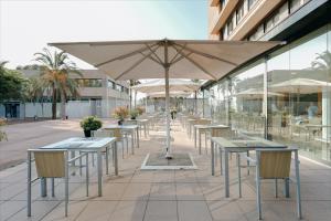 une rangée de tables et de chaises avec un parasol dans l'établissement Hesperia Barcelona Del Mar, à Barcelone