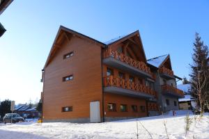 um grande edifício de madeira com uma varanda na neve em Apartmán Olaf Tatranská Lomnica em Tatranská Lomnica