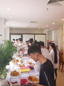 un grupo de personas de pie alrededor de una larga mesa con comida en Long Anh Hotel, en Thanh Hóa