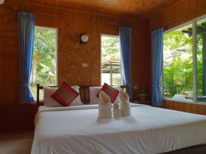 a bedroom with a white bed with pillows and windows at Baan Suan Hill Resort in Ban Tha Khun