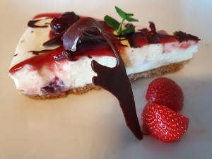 a piece of cheesecake with chocolate sauce and strawberries at Westland Hotel in Lindås