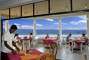un hombre parado en una mesa en un restaurante con el océano en Oasey Beach Hotel, en Bentota