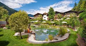 an exterior view of a resort with a pond at Alpwellhotel Burggräfler in Tesimo