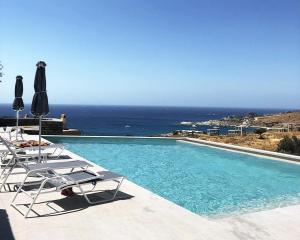 a swimming pool with chairs and umbrellas and the ocean at modern apartment with a sea view and swimming pool in Koundouros in Koundouros