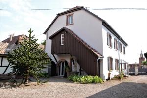 une maison blanche et noire avec un arbre en face dans l'établissement Ferme les Iris, à Issenheim