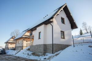a white house with a black roof in the snow at DOMKI NA WIERCHU in Biały Dunajec