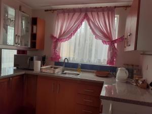 una cocina con fregadero y una ventana con cortinas rosas en Casa en La Serena, en La Serena