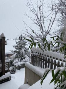 un patio cubierto de nieve con una valla y árboles en Maison Caramel, en Landry