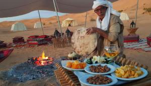 a man standing in front of a table with food and a fire at CAMP ABDELMOULA in Douz