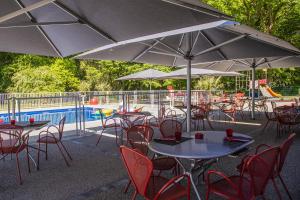 - un groupe de tables et de chaises avec parasols à côté d'une piscine dans l'établissement Kyriad Montchanin le Creusot, à Montchanin