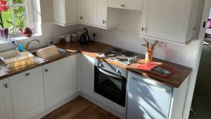 a kitchen with white cabinets and a stove and a sink at Hayloft Cottage - Dog Friendly With Private Garden in Sidmouth