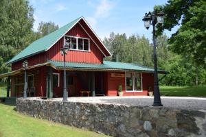 a red cabin with a green roof and a street light at Lazdkalni in Ķimale
