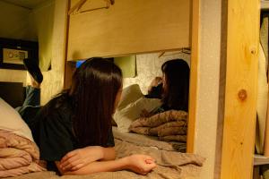 two girls sitting on bunk beds looking in a mirror at HOSTEL WASABI Nagoya Ekimae in Nagoya