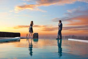 a man and a woman standing next to a swimming pool at Thermes Luxury Villas And Spa in Megalokhori