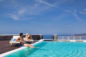 a man and a woman sitting in a chair next to a swimming pool at Thermes Luxury Villas And Spa in Megalochori