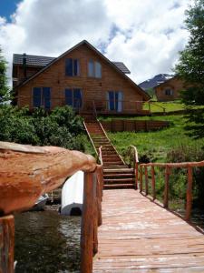 un paseo marítimo de madera que conduce a una casa con un edificio en Lodge de Montaña Lago Monreal, en El Blanco
