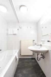 La salle de bains blanche est pourvue d'un lavabo et d'une baignoire. dans l'établissement Hotel Hölzer Bräu by Lehmann Hotels, à Ebersberg