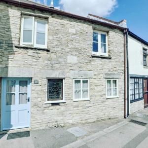 una antigua casa de piedra con una puerta y ventanas blancas en Cosy Little Hyde Cottage, Swanage, en Swanage