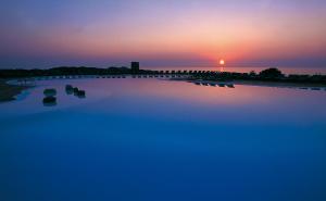 einen Pool mit Wasser und Sonnenuntergang im Hintergrund in der Unterkunft Hotel Relax Torreruja Thalasso & Spa in Isola Rossa