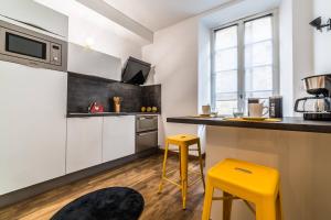 une cuisine avec des placards blancs et des tabourets jaunes dans l'établissement BLAISE RAYNAL #1 - Appartement coquet - 2 personnes, à Brive-la-Gaillarde