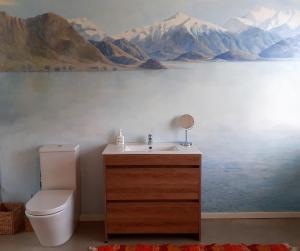 a bathroom with a toilet and a painting of mountains at The Hidden Spring in Wanaka