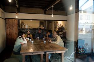 een groep mensen die rond een houten tafel zitten bij 1166 Backpackers in Nagano