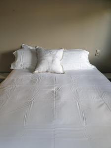 een wit bed met witte lakens en kussens bij Tron Central in Hamilton