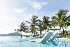uma piscina com cadeiras e palmeiras e o oceano em The Ocean Residence Langkawi em Kuah