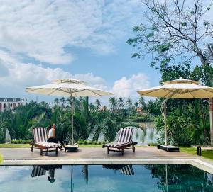a woman sitting in chairs next to a pool with umbrellas at Ylang Garden Villa in Hoi An