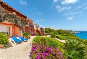a house with two blue chairs and flowers at Residencial Playa Mar in Cala Mendia