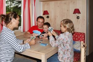een man en twee kinderen die met kaarten aan tafel spelen bij Camping le Nid du Parc in Villars-les-Dombes