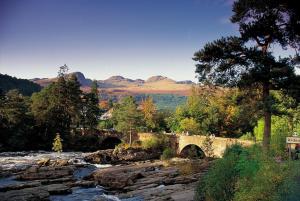 a bridge over a river with mountains in the background at Luxury woodland Alder Lodge in Killin