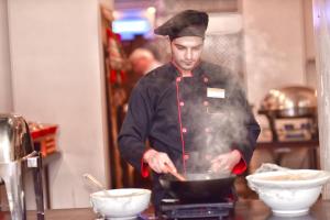 a man cooking food in a pan on a stove at La Maison Hotel in Wadi Musa