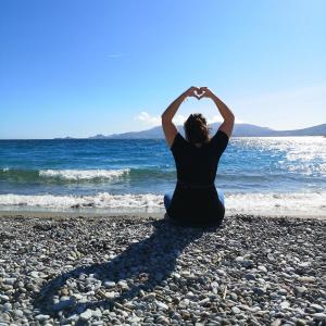 Eine Frau am Strand, die ein Herz mit den Händen macht. in der Unterkunft Haraki Village in Charaki