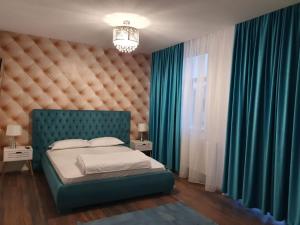 Schlafzimmer mit einem Bett mit blauem Kopfteil und grünen Vorhängen in der Unterkunft GARSONIERRE CENTRAL LUXURY in Târgu Jiu
