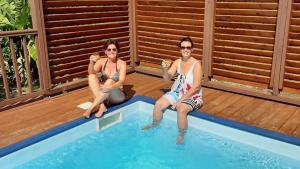 two women sitting on the edge of a swimming pool at Lili bungalows in Capesterre-de-Marie-Galante