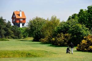 a man walking a dog on a golf course with a house in the background at Thorpeness Golf Club and Hotel in Thorpeness