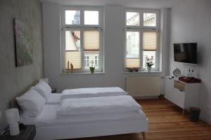 a white bedroom with two beds and windows at Bilderbuchcafe - Pension Markt 7 in Havelberg